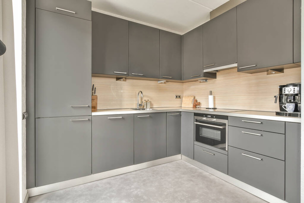 Bu modern görünümlü mutfağın tezgahlarında gri dolapları ve beyaz tezgahları olan bir mutfak doğal ışıkla aydınlanıyor. - Fotoğraf, Görsel