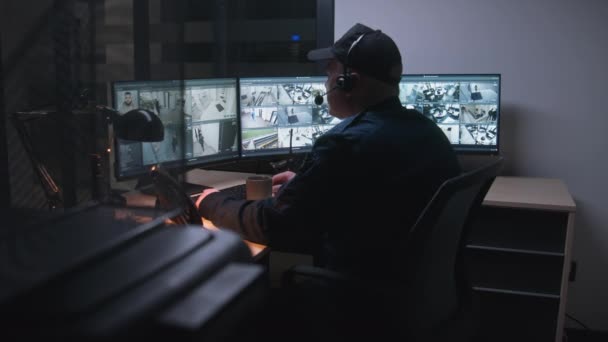 Sicherheitsmitarbeiter mit Headset steuern nachts Überwachungskameras im Büro, nutzen Computer. Hightech-Programm mit Überwachungskameras auf Bildschirmen. Modernes Sicherheitssystem und soziales Sicherheitskonzept. - Filmmaterial, Video