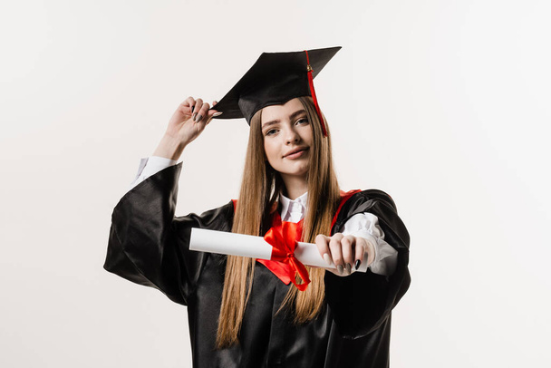 Masters degree diploma with red ribbon in hands of graduate girl in black graduation gown on white background. Graduate girl is graduating high school and celebrating academic achievement - Foto, Imagen