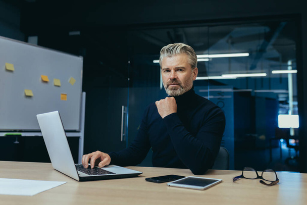 Portrait of serious gray haired boss, man looking at camera thinking, mature businessman inside office working at desk using laptop at work. - Foto, Imagem