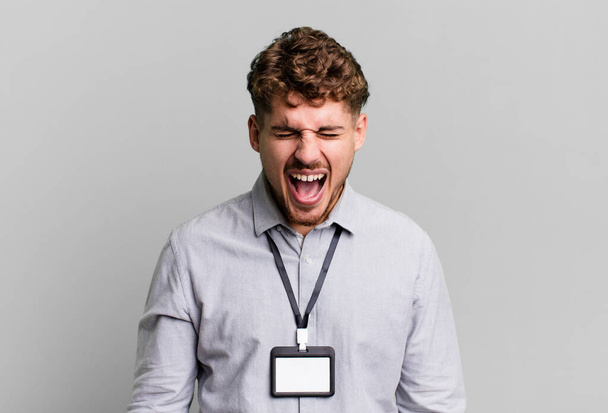 young adult caucasian man shouting aggressively, looking very angry. blank accreditation pass card id concept - Photo, image