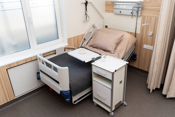Geräumige Krankenhausstation, am Fenster steht ein Bett, das angehoben und abgesenkt werden kann. Ein bequemes Bett für eine bequeme Erholung und Rehabilitation. - Foto, Bild
