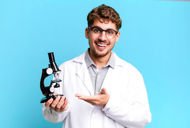 young adult caucasian man smiling cheerfully, feeling happy and showing a concept. scients laboratory student with a microscope concept - Foto, immagini