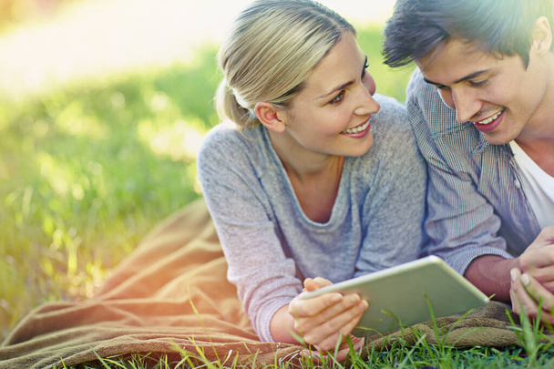 Ze hebben een zonnige verbinding. een gelukkig jong paar liggend op het gras en met behulp van een digitale tablet samen - Foto, afbeelding