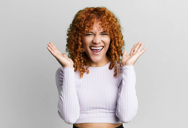 redhair pretty woman looking happy and excited, shocked with an unexpected surprise with both hands open next to face - 写真・画像