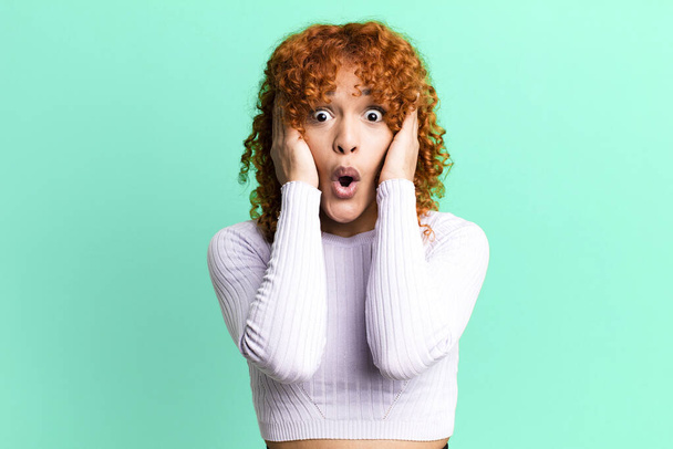 redhair pretty woman looking unpleasantly shocked, scared or worried, mouth wide open and covering both ears with hands - Fotoğraf, Görsel