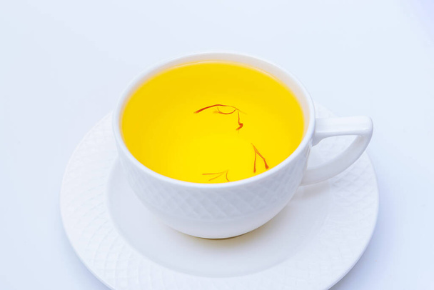 Шафрановый чай в белой чашке на белом фоне. Благоухающий здоровый напиток. - Фото, изображение