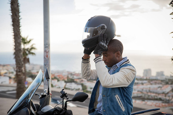 African American motorcyclist wears a helmet while sitting on his motorcycle - Zdjęcie, obraz
