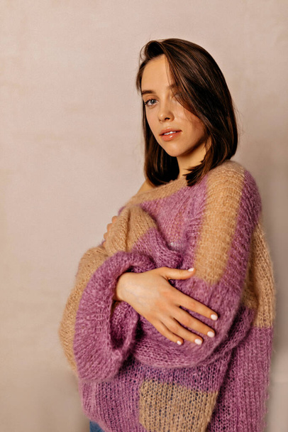 Elegant adorable cute lady with short hairstyle and nude make up is wearing knitted brightful sweater is crossed arms on waist and looking to camera over isolated background. Beauty concept  - Foto, afbeelding