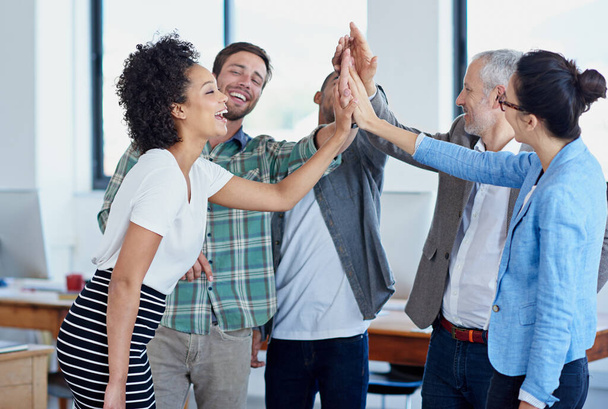 Great job everybody. a group of happy coworkers high-fiving while standing in an office - Foto, imagen