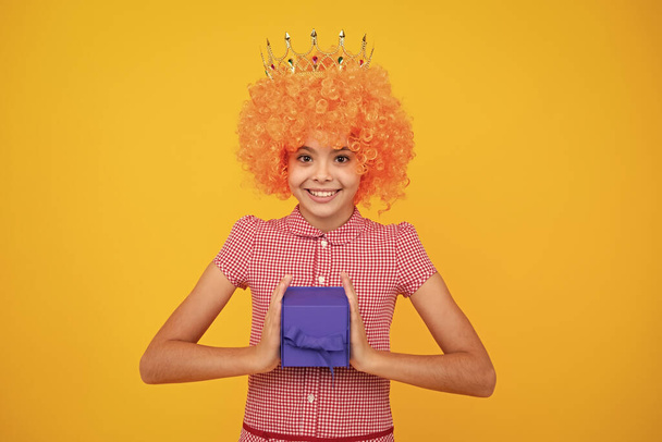 Funny princess in wig and crown. Portrait of teenager child girl 12, 13, 14, years old holding Christmas gift box. Teen giving birthday gift - Photo, Image