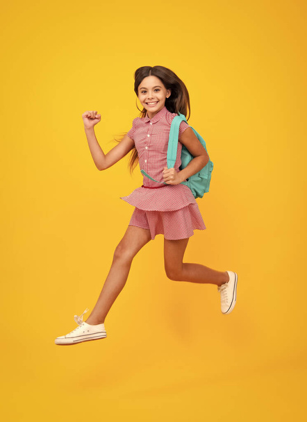 Schoolgirl in school uniform with school bag. Schoolchild, teen student hold backpack on yellow isolated background. Crazy run and jump - Photo, Image