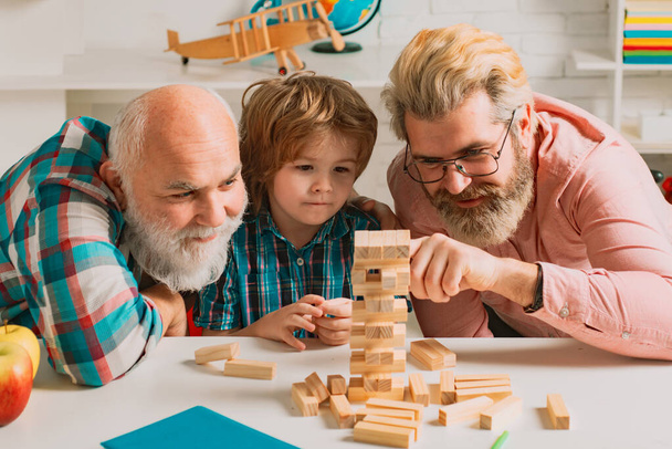 Grandfather father and pupil son smiling against home background. Happy generational muti three generation men family portrait. Jenga game at home - Foto, afbeelding