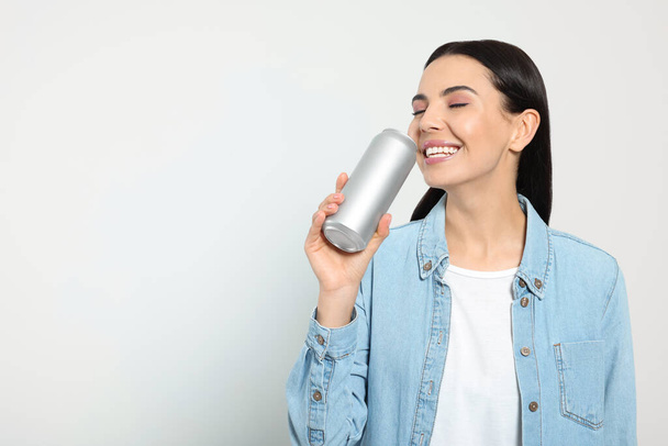 Beautiful happy woman drinking from beverage can on light grey background. Space for text - Foto, afbeelding