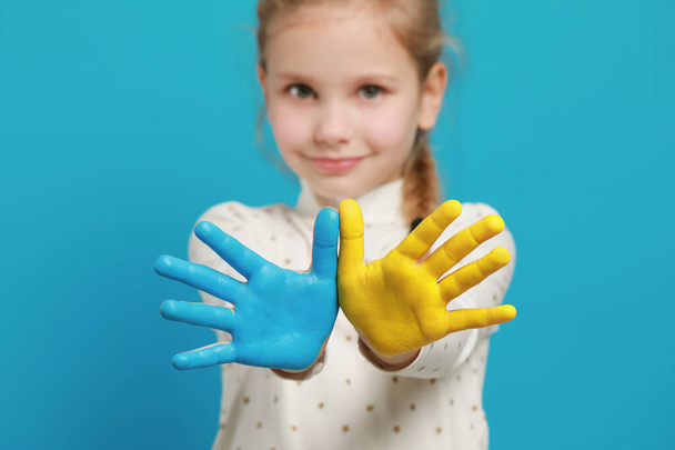 Little girl with hands painted in Ukrainian flag colors against light blue background, focus on palms. Love Ukraine concept - Фото, зображення