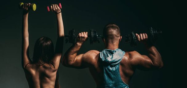 Sexy sport couple exercising with dumbbell. Muscular man with naked body, fitness woman with dumbbells on a dark background, back view. Slim sexy girl with strong muscular man workout - Foto, Bild
