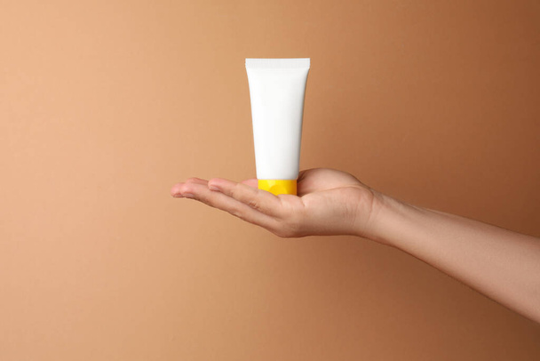 Woman holding tube of face cream on beige background, closeup. Space for text - Foto, afbeelding