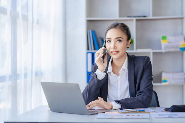 Freiberufliche asiatische Geschäftsfrau telefoniert und arbeitet mit Laptop-Computer und Finanzdiagramm Dokument verwalten ihr Geschäft bei der Arbeit Machen Sie einen Plan über Finanzberichte im Büro. - Foto, Bild