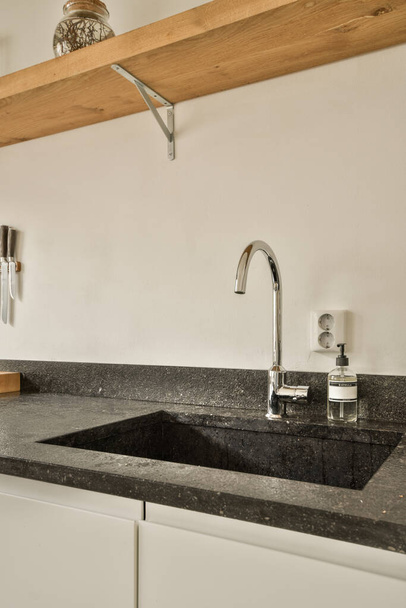 Beyaz bir odada, üzerinde siyah granit tezgah olan bir mutfak lavabosu ve musluk. - Fotoğraf, Görsel