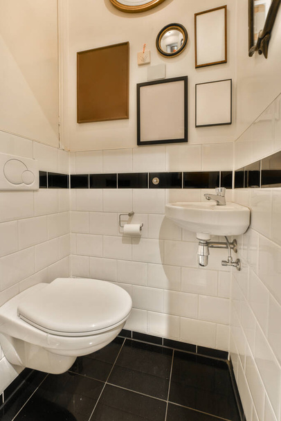 Yerde siyah beyaz fayanslar, klozetin üstündeki ayna ve duvarda asılı çerçeveli resimler olan bir banyo. - Fotoğraf, Görsel