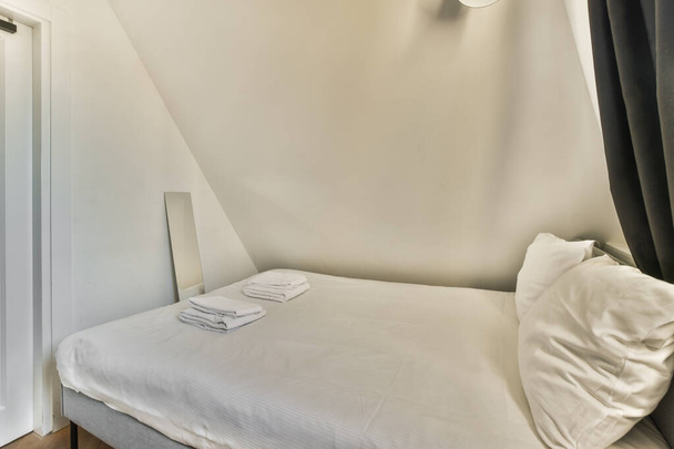 een bed in een kamer met witte muren en zwarte gordijnen opknoping aan de muur erachter is een open deur - Foto, afbeelding
