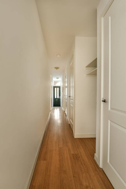 um longo corredor com pisos de madeira e paredes brancas em um prédio de apartamentos, levado da porta da frente para a esquerda - Foto, Imagem