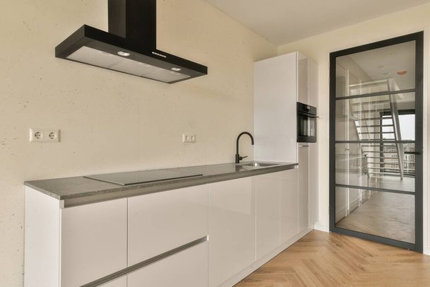 una cucina moderna con armadi bianchi e ripiani neri a parete, di fronte a una porta a vetri aperti - Foto, immagini