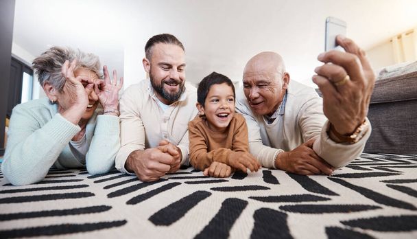 Χαρούμενη μεγάλη οικογένεια, χαμόγελο και να λάβει selfie στο σπίτι σαλόνι για τη μνήμη ή τα μέσα κοινωνικής δικτύωσης. Φωτογράφος φροντίδα, κωμικό πρόσωπο και ο πατέρας, παππούδες και το παιδί στο πάτωμα τη λήψη φωτογραφιών, συγκόλληση ή γέλιο - Φωτογραφία, εικόνα