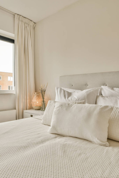 un letto con lenzuola bianche e cuscini in una piccola stanza accanto a una finestra illuminata dal sole - Foto, immagini