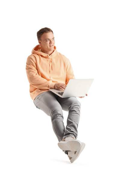 Jonge kerel met behulp van laptop in stoel op witte achtergrond - Foto, afbeelding
