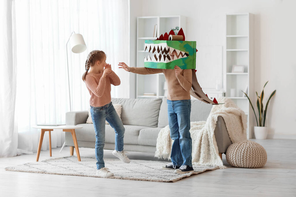 Налякана маленька дівчинка і її брат в картонному костюмі динозавра вдома
 - Фото, зображення