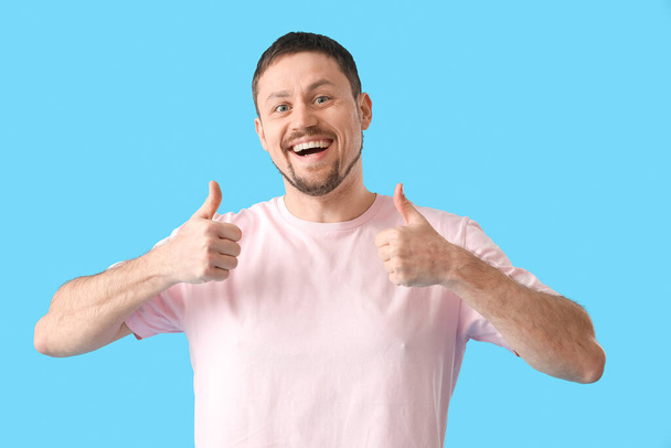 Hezký muž v tričku ukazující palce nahoru na modrém pozadí - Fotografie, Obrázek