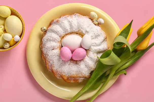 Тарелка с вкусным пасхальным тортом, цветы тюльпана и яйца на розовом фоне - Фото, изображение
