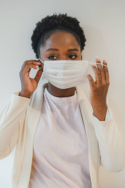 Молода афроамериканська жінка вдягає багаторазову медичну маску, щоб запобігти зараженню вірусом корони на білому тлі. Портрет студії - Фото, зображення