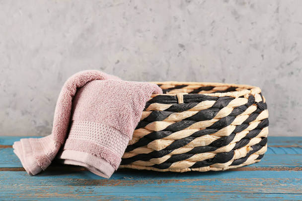 Wicker basket with soft towel on blue wooden table near grey wall - 写真・画像