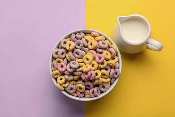 Ciotola di anelli di cereali e brocca con latte su sfondo colorato - Foto, immagini