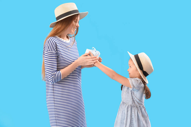 Χαριτωμένο κοριτσάκι χαιρετώντας τη μητέρα της με δώρο σε μπλε φόντο - Φωτογραφία, εικόνα
