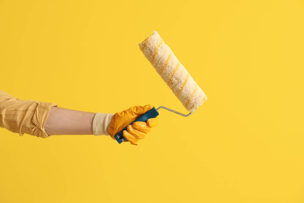 Worker with paint roller on yellow background - Foto, afbeelding