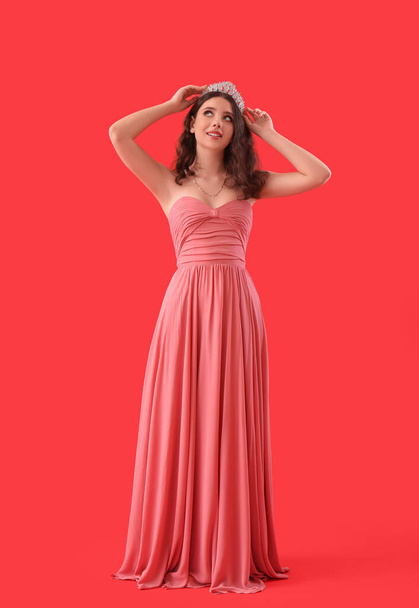 Teenage girl in tiara and prom dress on red background - Photo, Image