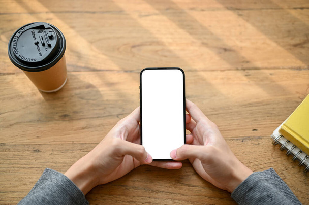 Widok z góry, męskie ręce piszące na smartfonie, korzystające z telefonu nad drewnianym stołem. smartphone biały ekran makieta - Zdjęcie, obraz