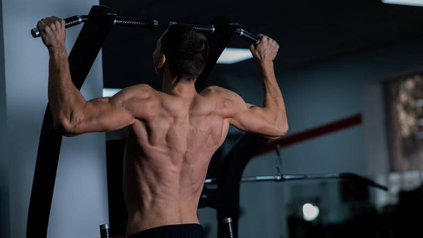 Back view of shirtless man with pull-ups in gym - Foto, Bild