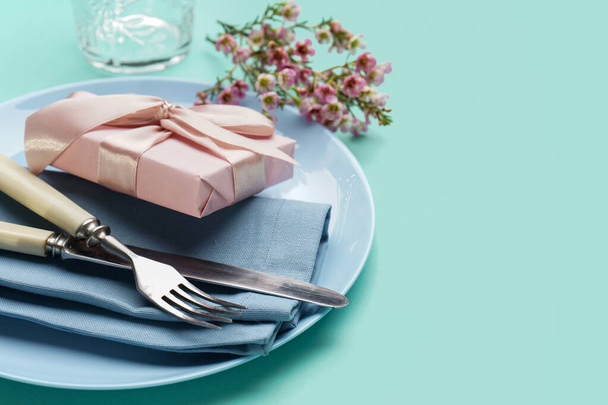 Table setting with gift box, cutlery and floral decor on turquoise background - Photo, Image