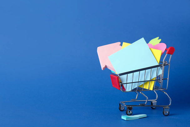Shopping cart with different sticky notes on blue background - Foto, Bild
