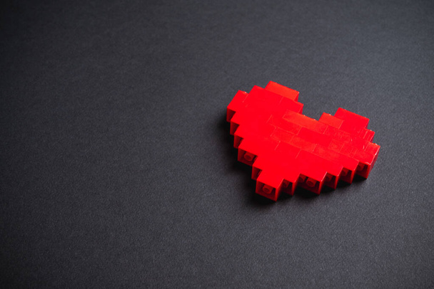 Red heart made of plastic bricks on a dark gray background - Valokuva, kuva