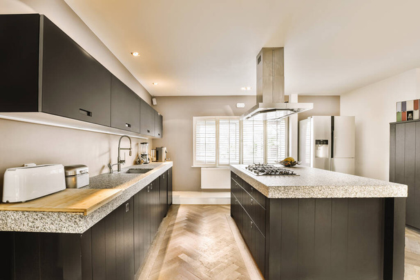 una cocina moderna con encimeras de granito y armarios negros, junto con pisos de madera en la parte media de la habitación - Foto, Imagen