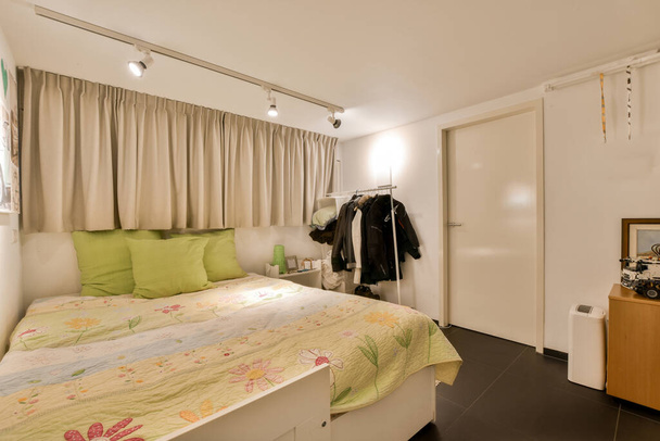 un dormitorio con una cama, vestidor y ropa colgando en la pared frente a la puerta de la habitación - Foto, imagen
