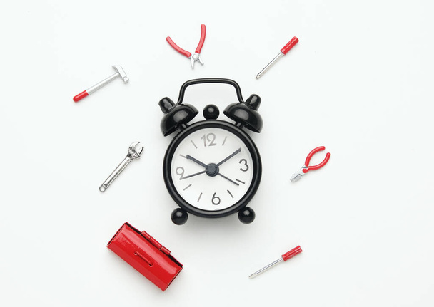 A flatlay picture of alarm clock with tools miniature on white background. Repairing time and fixing - Fotoğraf, Görsel