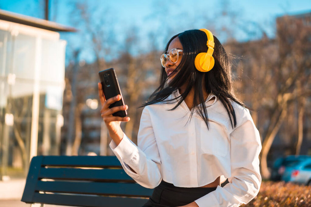 African american woman listening to music with headphones at sunset in the city, copy paste - Foto, Bild