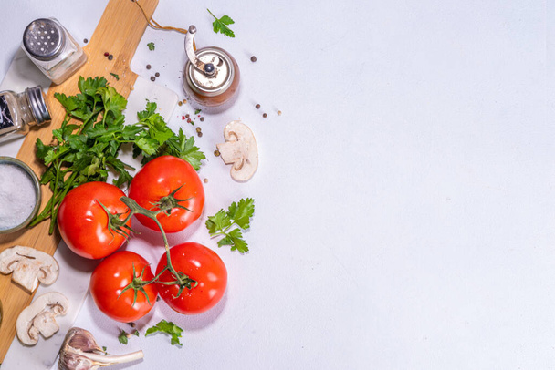 Cooking background with vegetable ingredients. Healthy dinner preparation flat lay, with fresh raw tomatoes, onion, garlic, herbs and greens, olive oil, salt, pepper seasonings, on white background  - Φωτογραφία, εικόνα