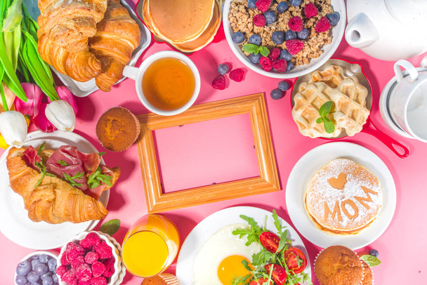 Moederdag Brunch restaurant uitnodiging concept. Diverse Moms Womans Day Menu achtergrond, met traditionele ontbijt en lunch eten en drinken set, met bloemen op zonnige roze achtergrond - Foto, afbeelding